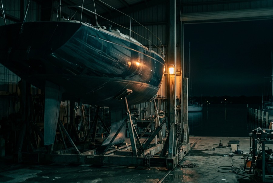 A boat hull under a work light in a dark boatyard workshop