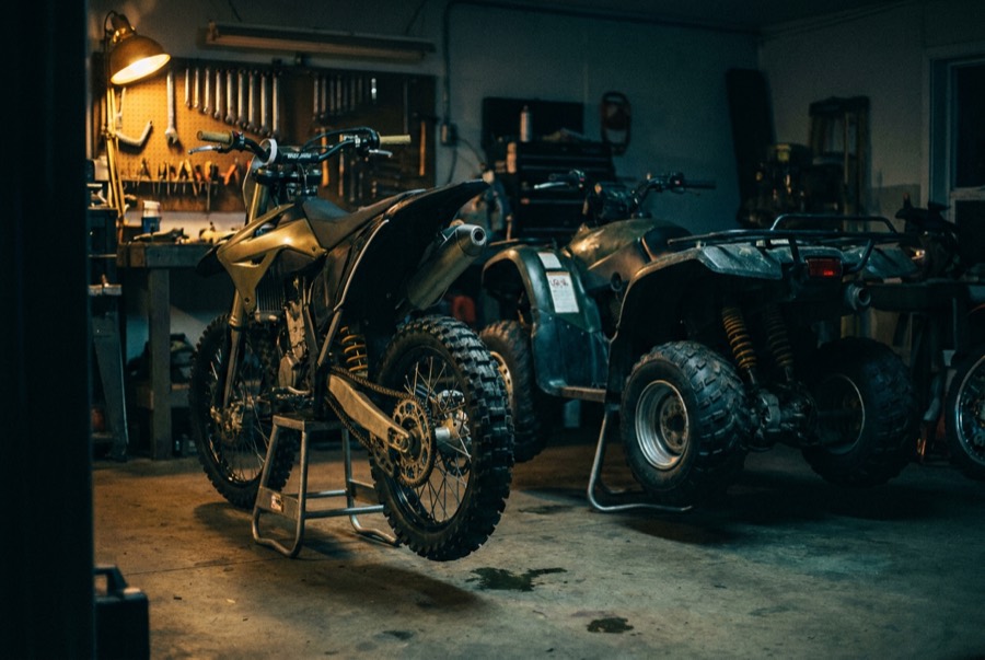 A dirt bike and ATV on stands in a dark powersports workshop